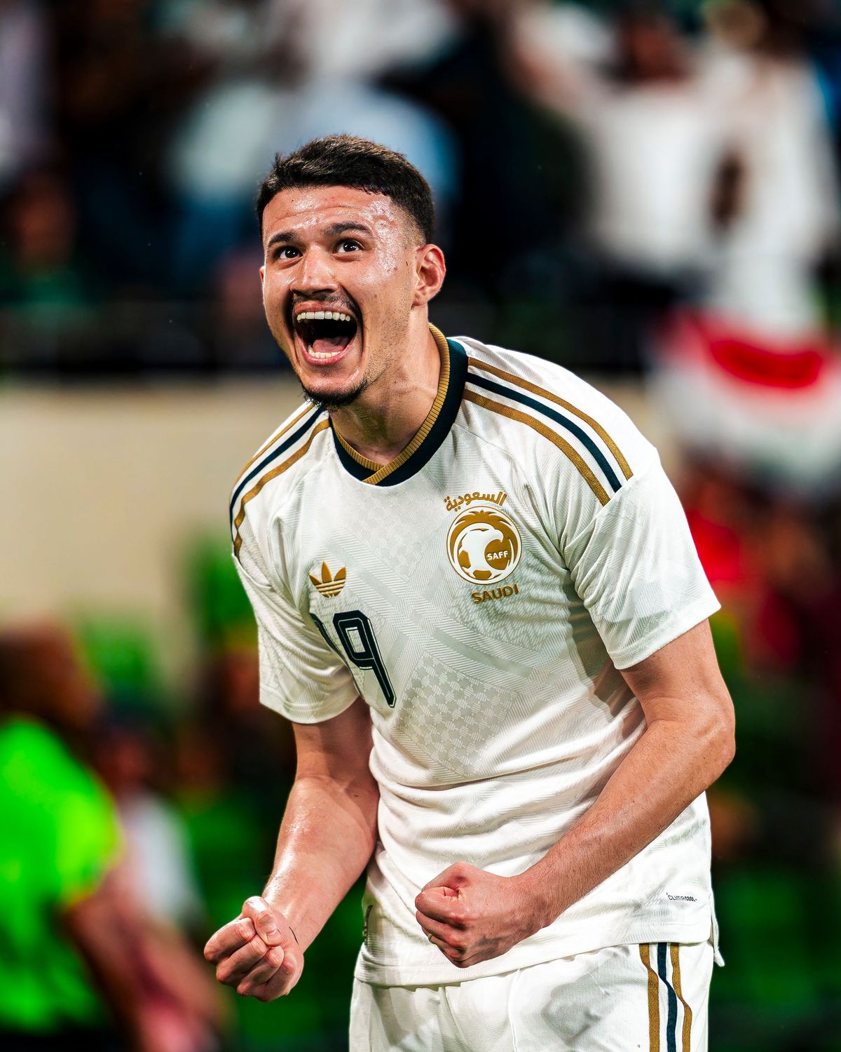 Soccer player in white and gold kit roaring toward the crowd after a goal