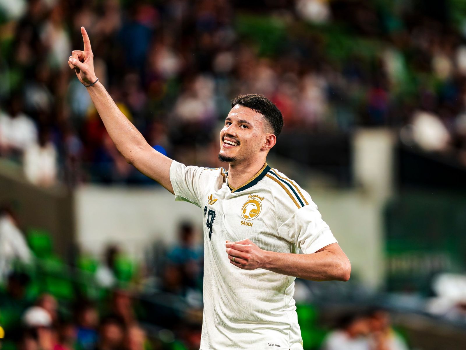 Soccer player in a white kit pointing to the sky after a goal