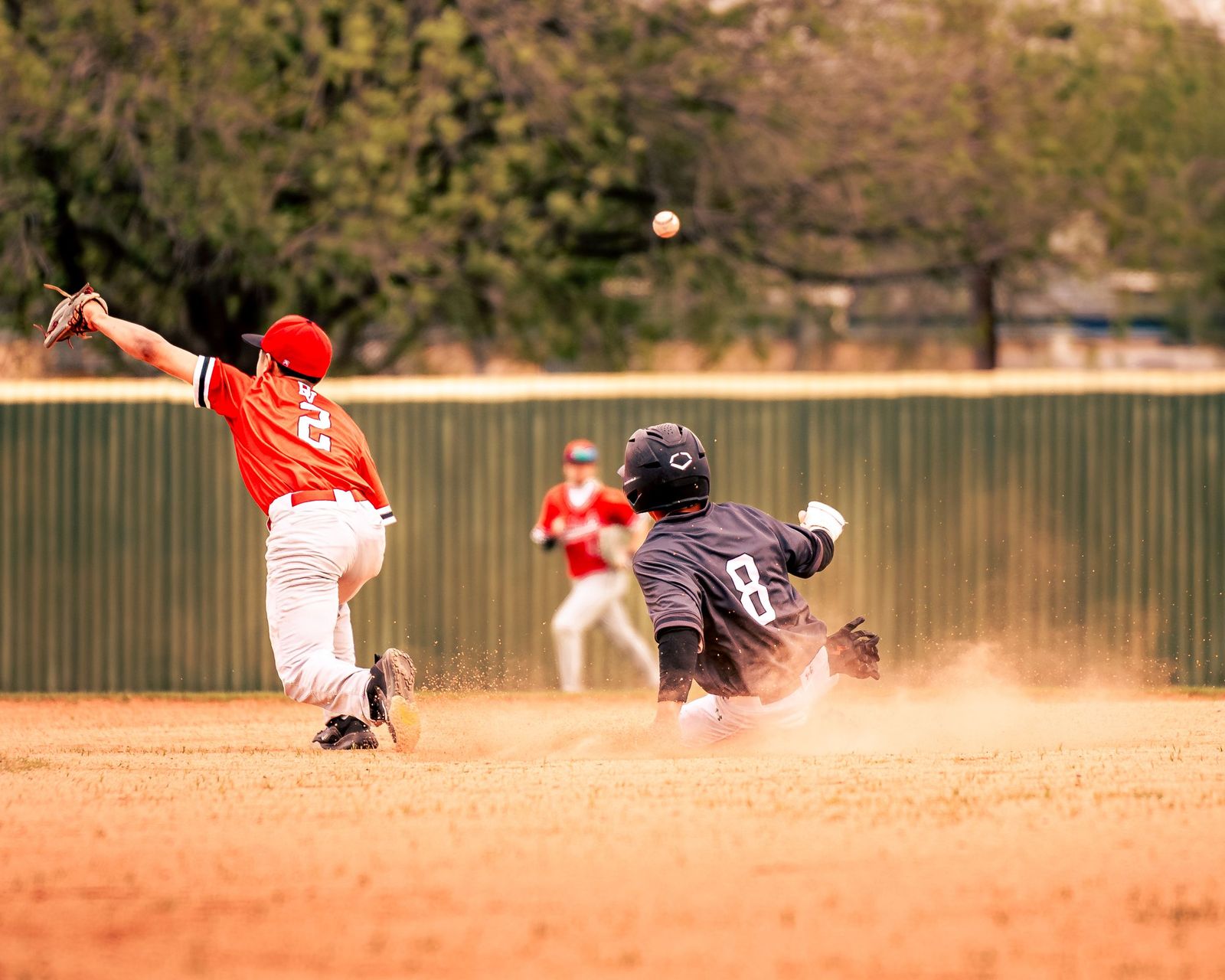 Infielder leaping for a throw as a runner slides in