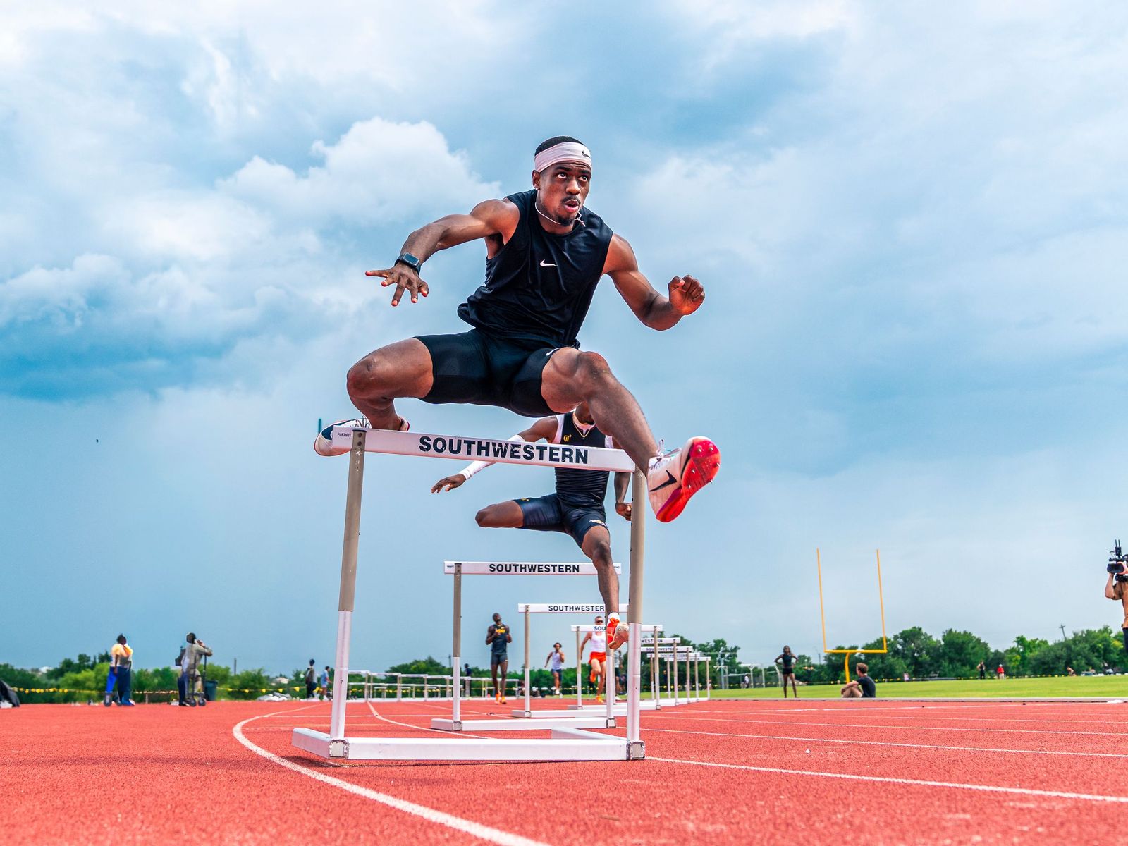 Hurdler mid-flight over a hurdle on a red track