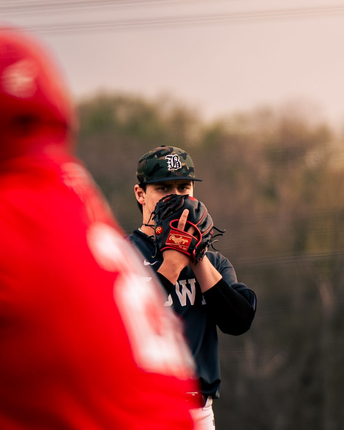Catcher in a red hoodie adjusting his mask