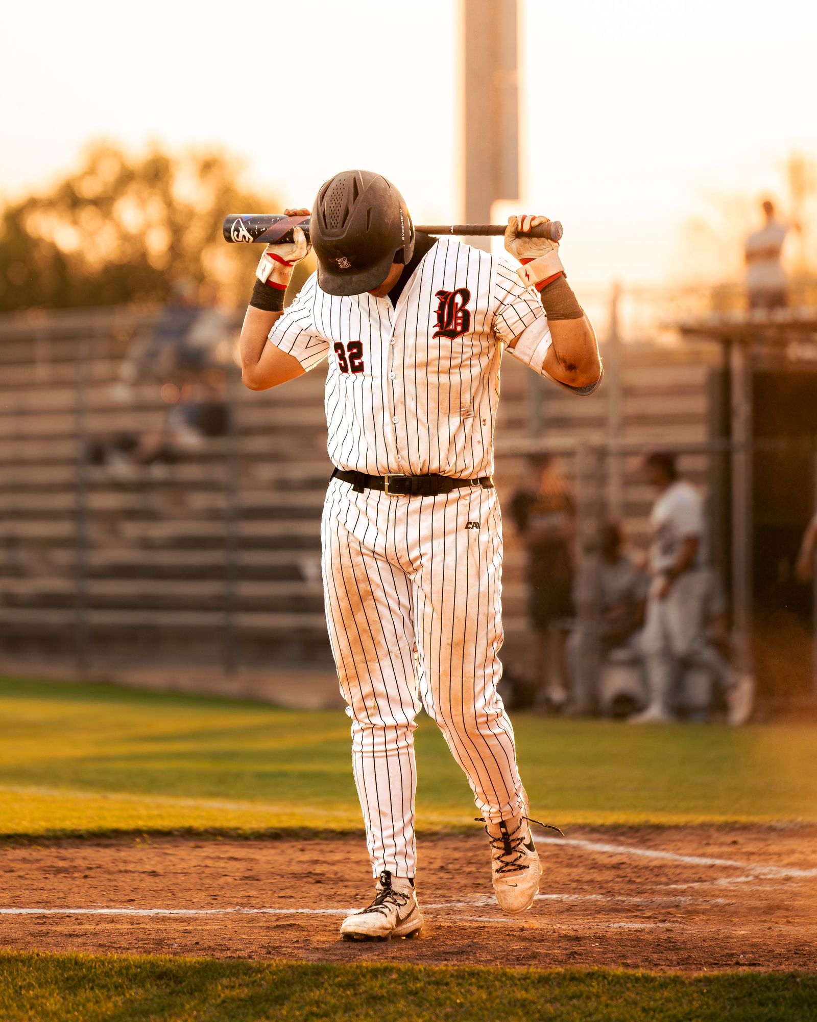 Batter resting the bat behind his neck at sunset