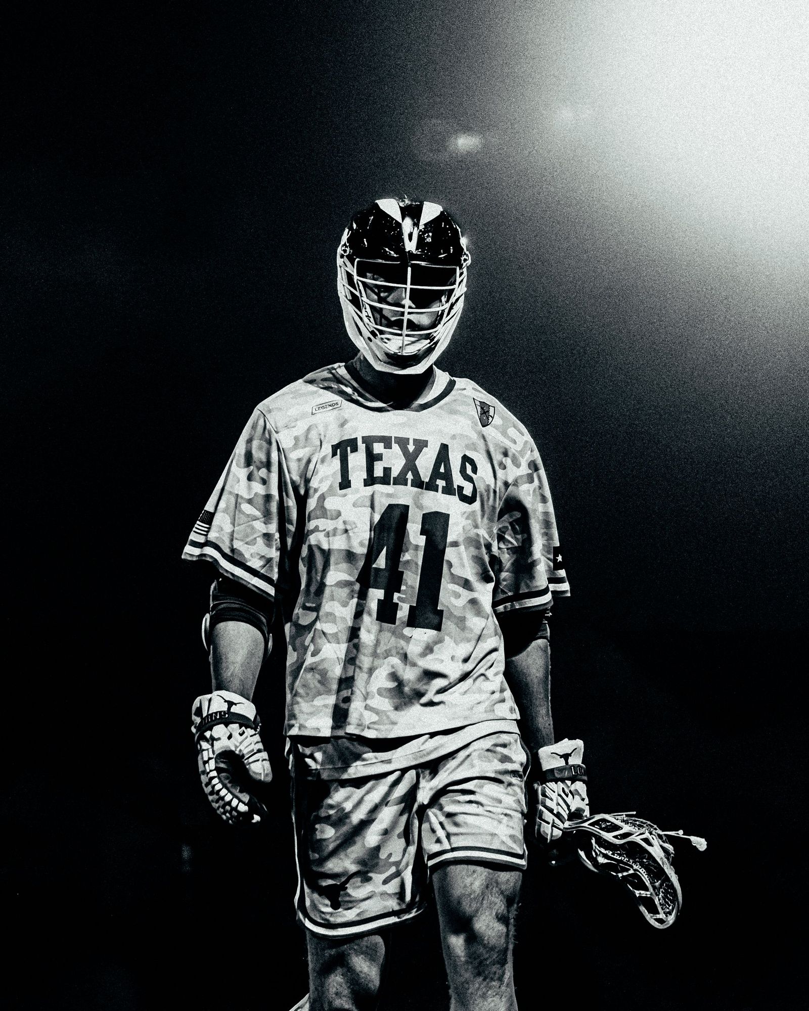 Texas lacrosse player in a camo uniform under stadium lights, black and white