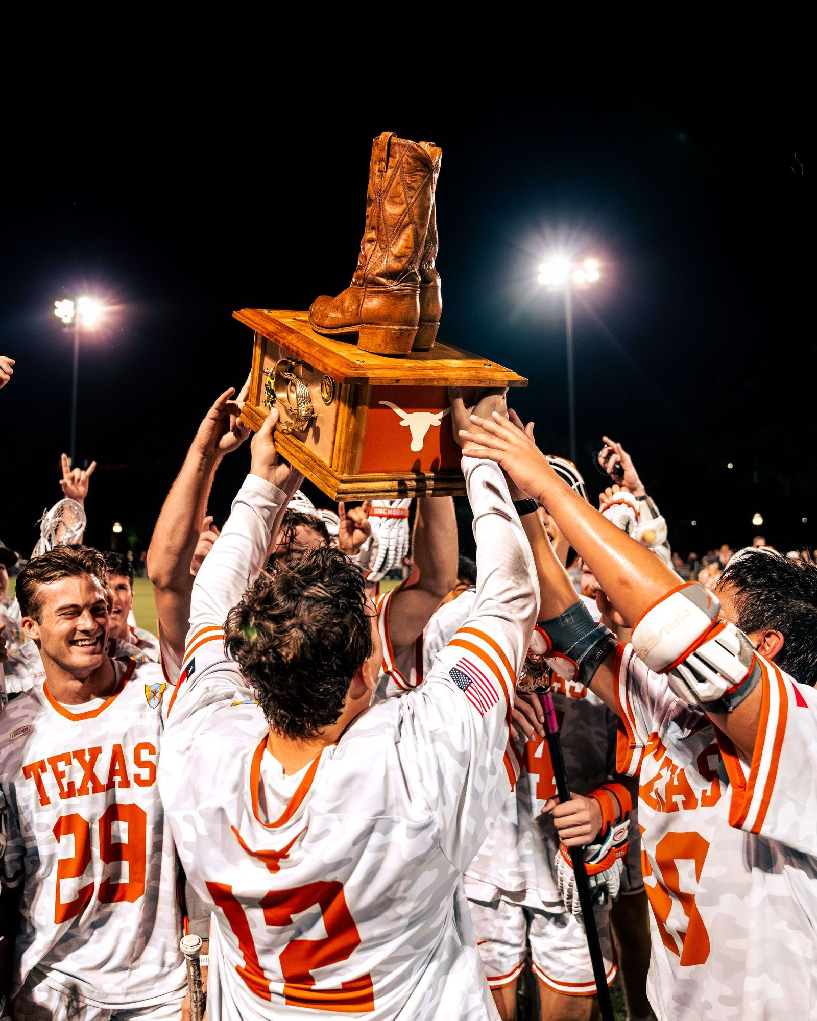 Texas lacrosse players hoisting a trophy at night