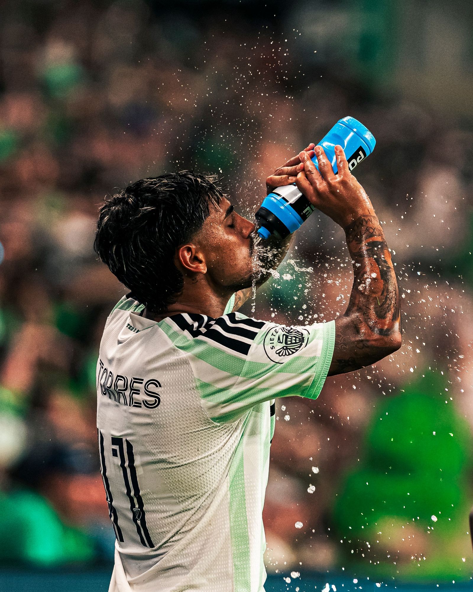 Austin FC player squeezing a water bottle over his face