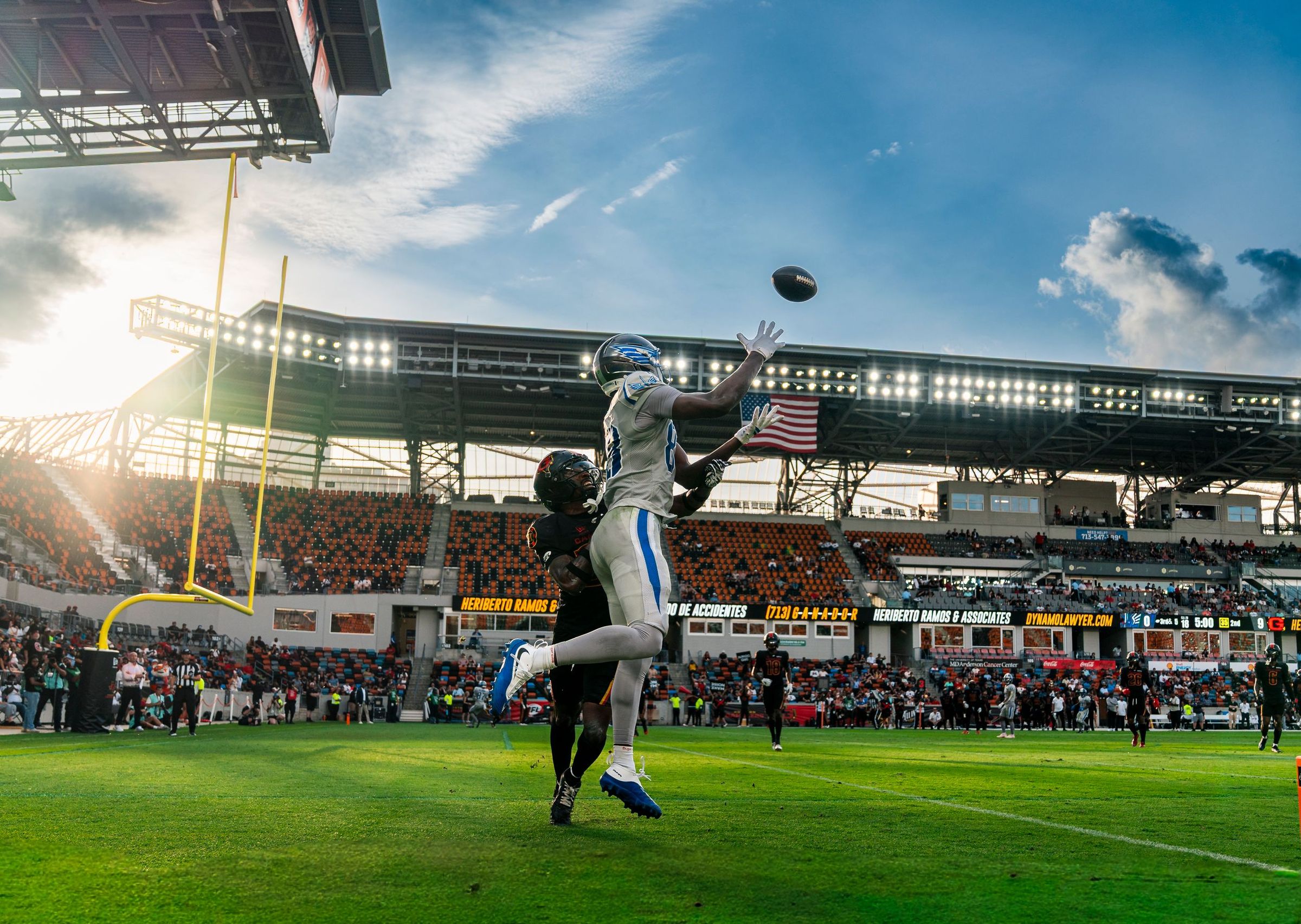 Receiver tracking a deep ball at sunset in front of a full stadium