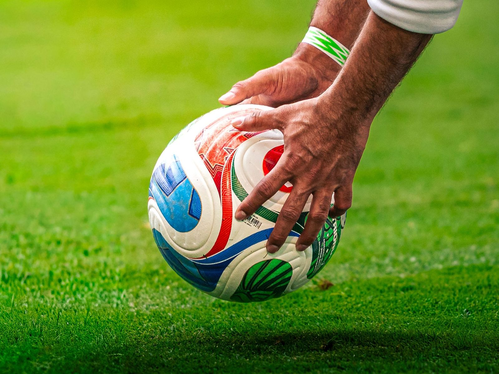 A hand placing a soccer ball on the grass