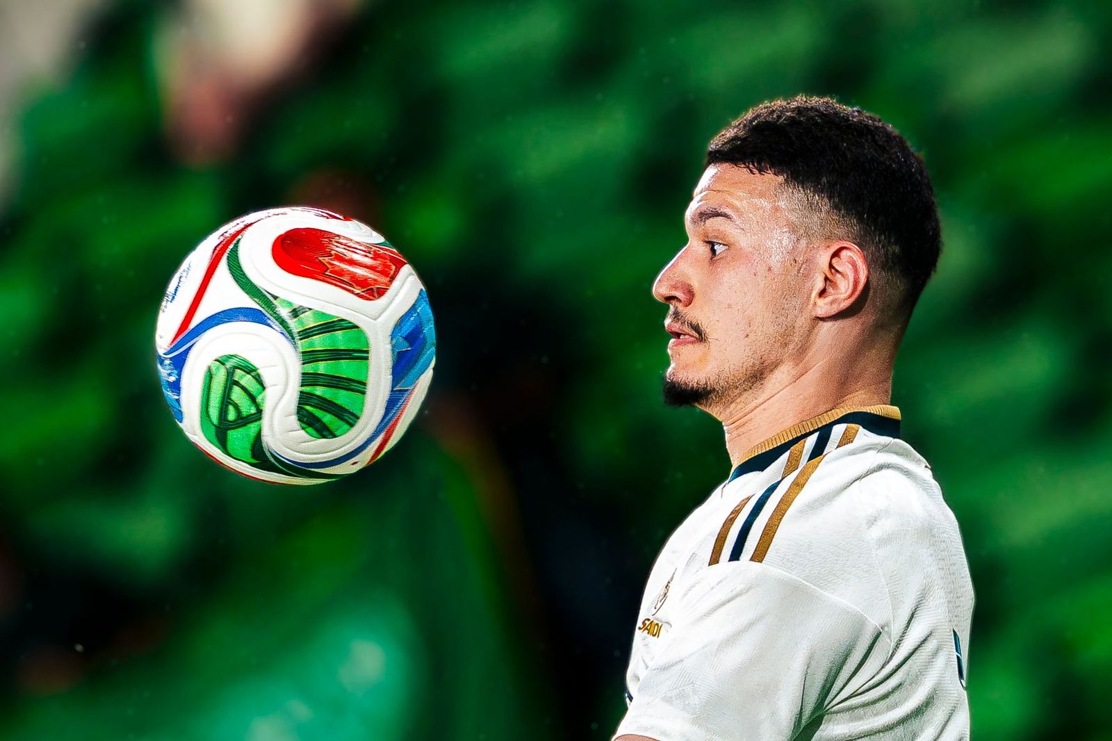 Soccer player in a white and gold kit with a ball at his feet