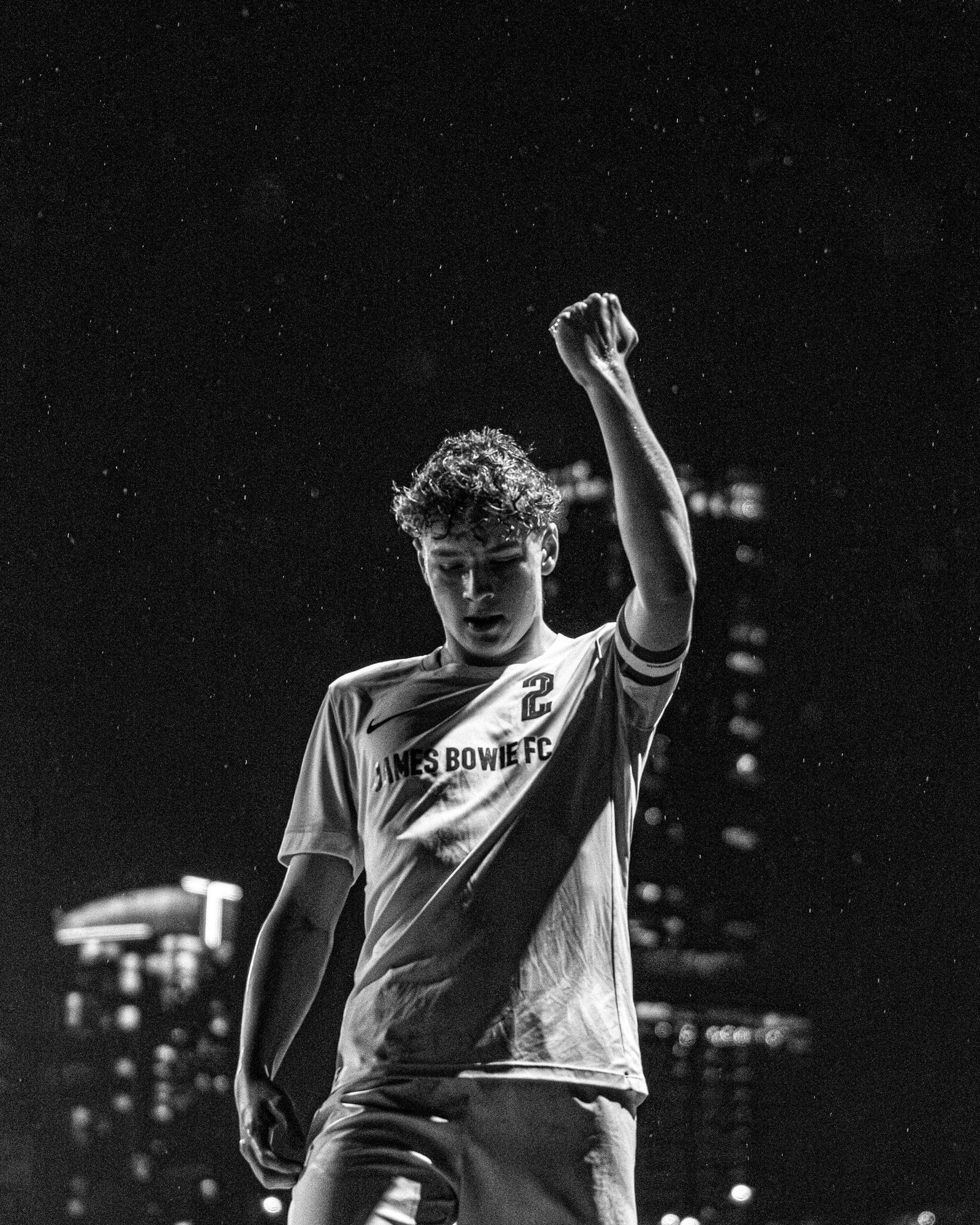 Player raising a fist against the city skyline at night, black and white