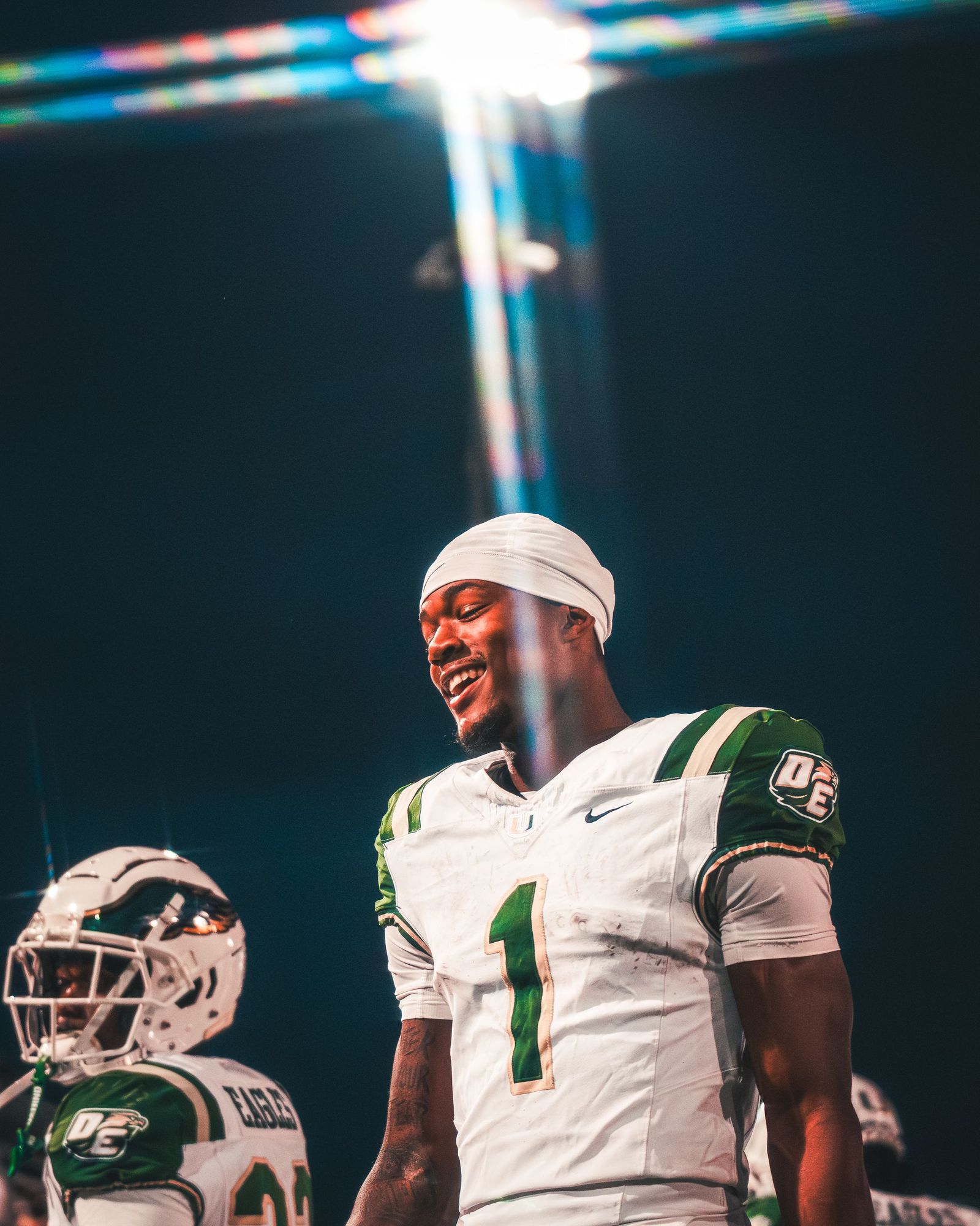 Football player in white and green with a headband smiling under the lights