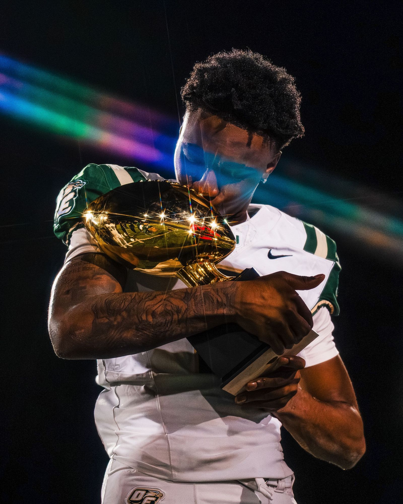 Football player hugging a gold championship trophy under stage lights