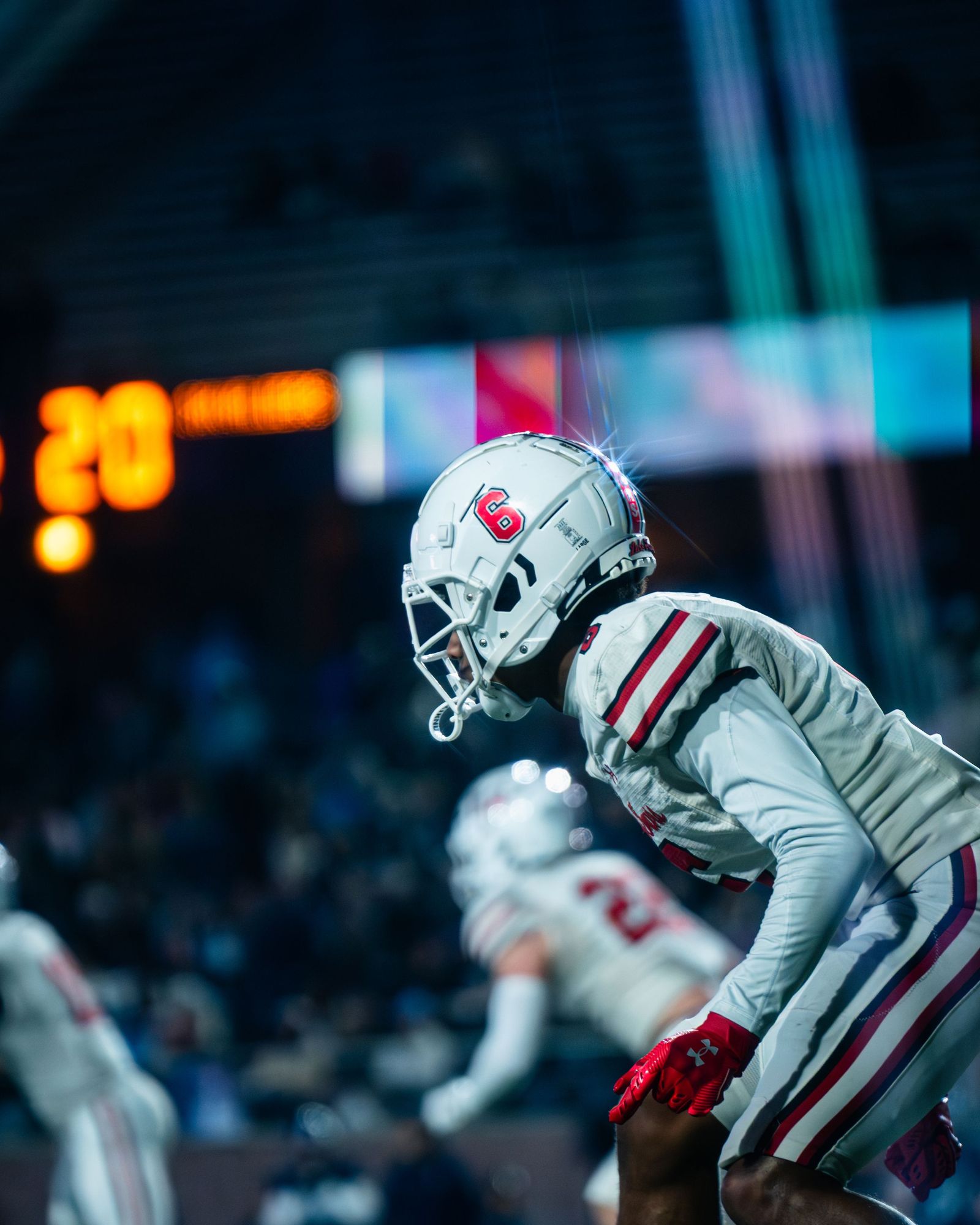 Lake Travis player in a red and white helmet leaping under stadium lights